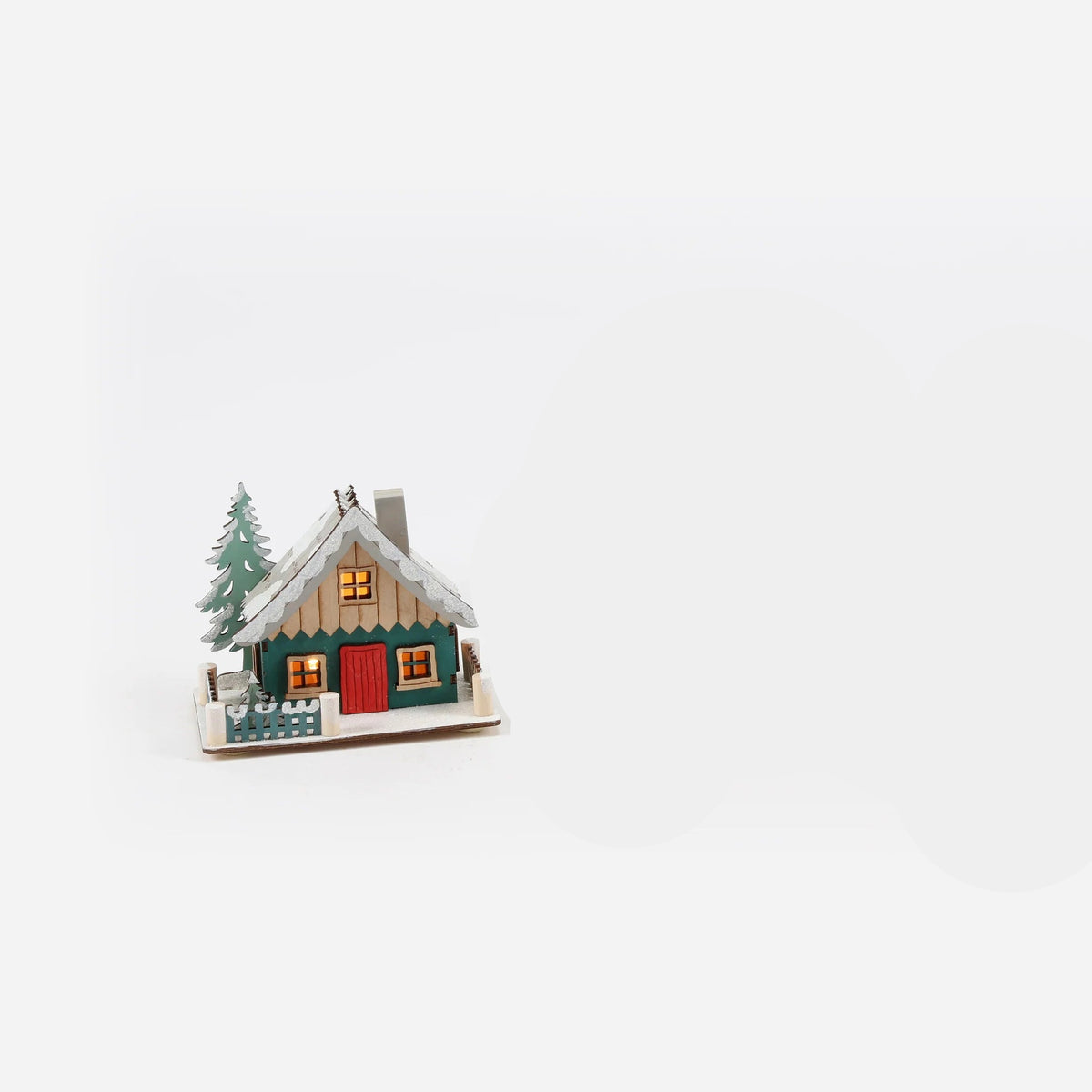 small green house ornaments design a a ski lodge with snow draping its grey roof,  a red front door, and a tree behind it