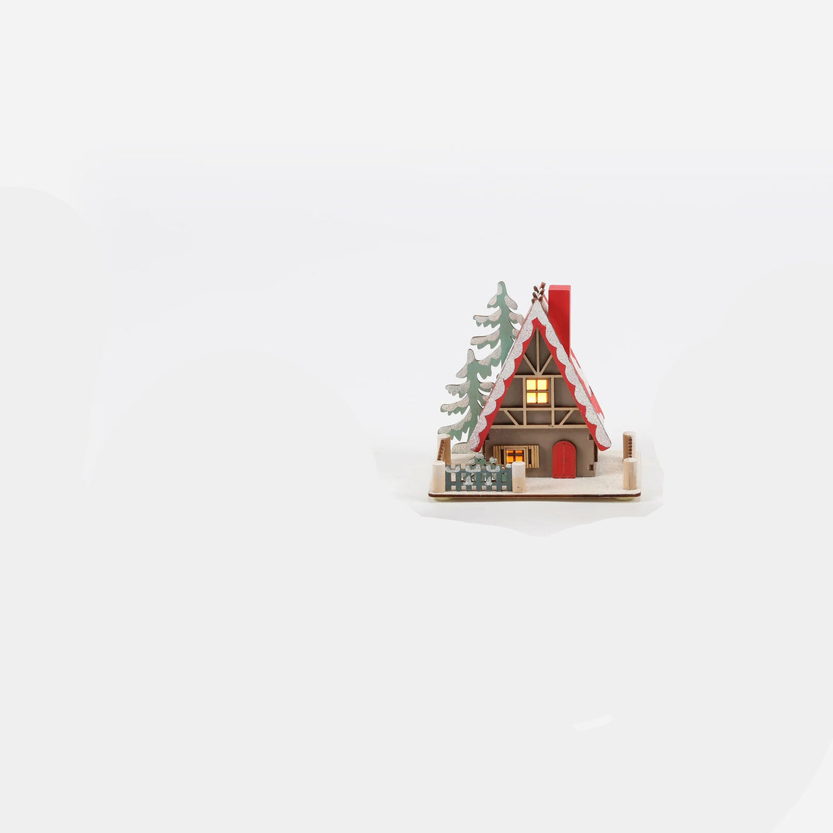 small brown A-frame ski lodge ornament with snow on its red roof, trees, and a little picket fence