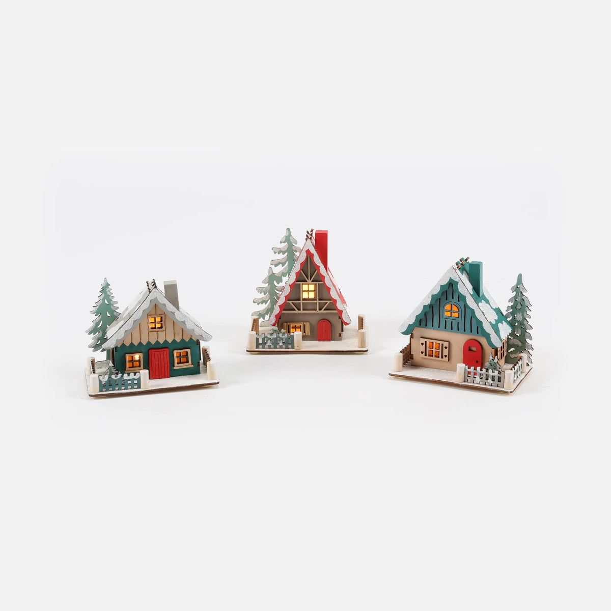 three decorative ski lodge ornaments with different colors and designs, each featuring a small tree and lightsin the windows.