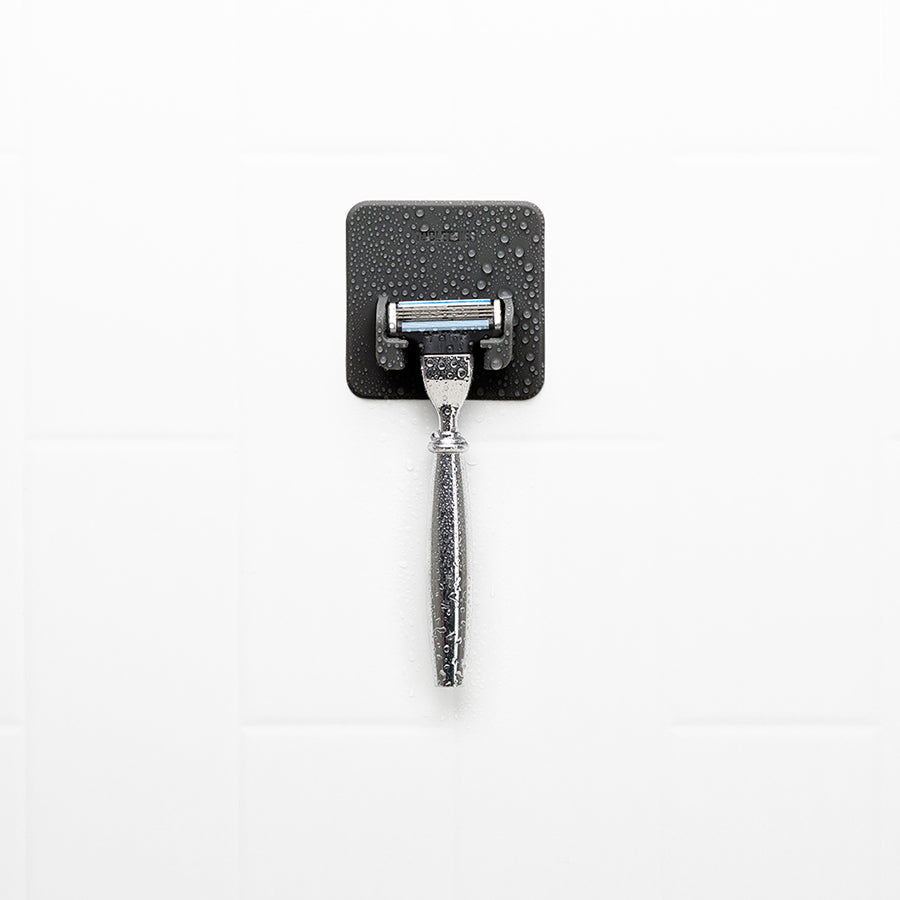 wet black silicone razor holder with a razor in it on a white tile background.