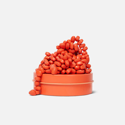 A collection of orange magnetic pebbles spilled out of a small orange container, arranged in a visually appealing pattern against a white background.