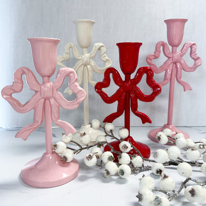 Pink, red, and white cast iron candle holders with bows on a tabletop with faux berry foliage.