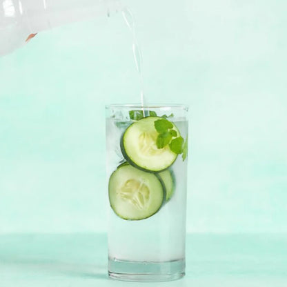 water being poured into a glass filled with ice, mint, and cucumber slices