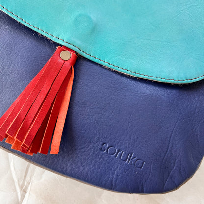 close-up of lola bag with turquoise flap with rusty colored tassel over a navy body.