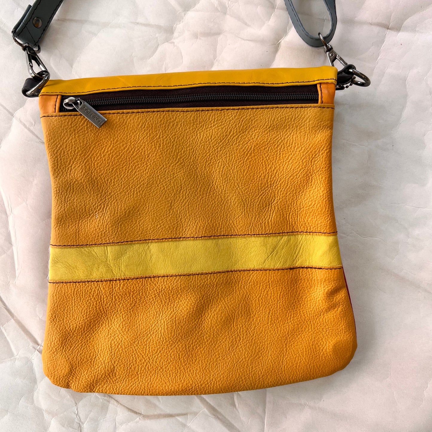 shades of yellow striped greta bag with zipper across the top.