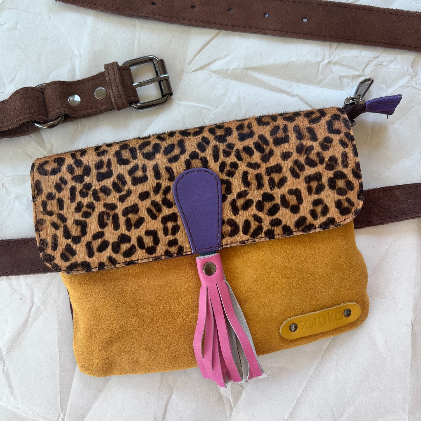 small square bag with yellow suede body, cheetah print flap with pink tassel, and brown belt.