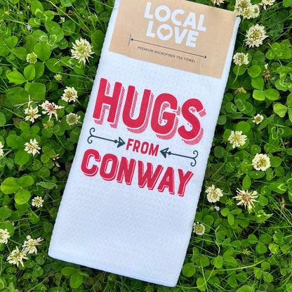 white towel with "hugs from conway" printed on it in red laying in a field of clovers.