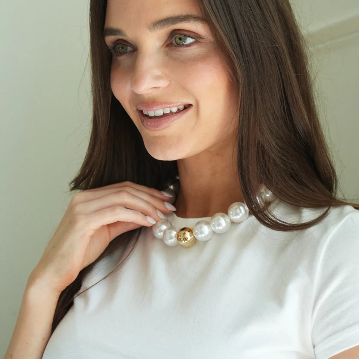 person wearing a chunky pearl necklace and a white tee shirt