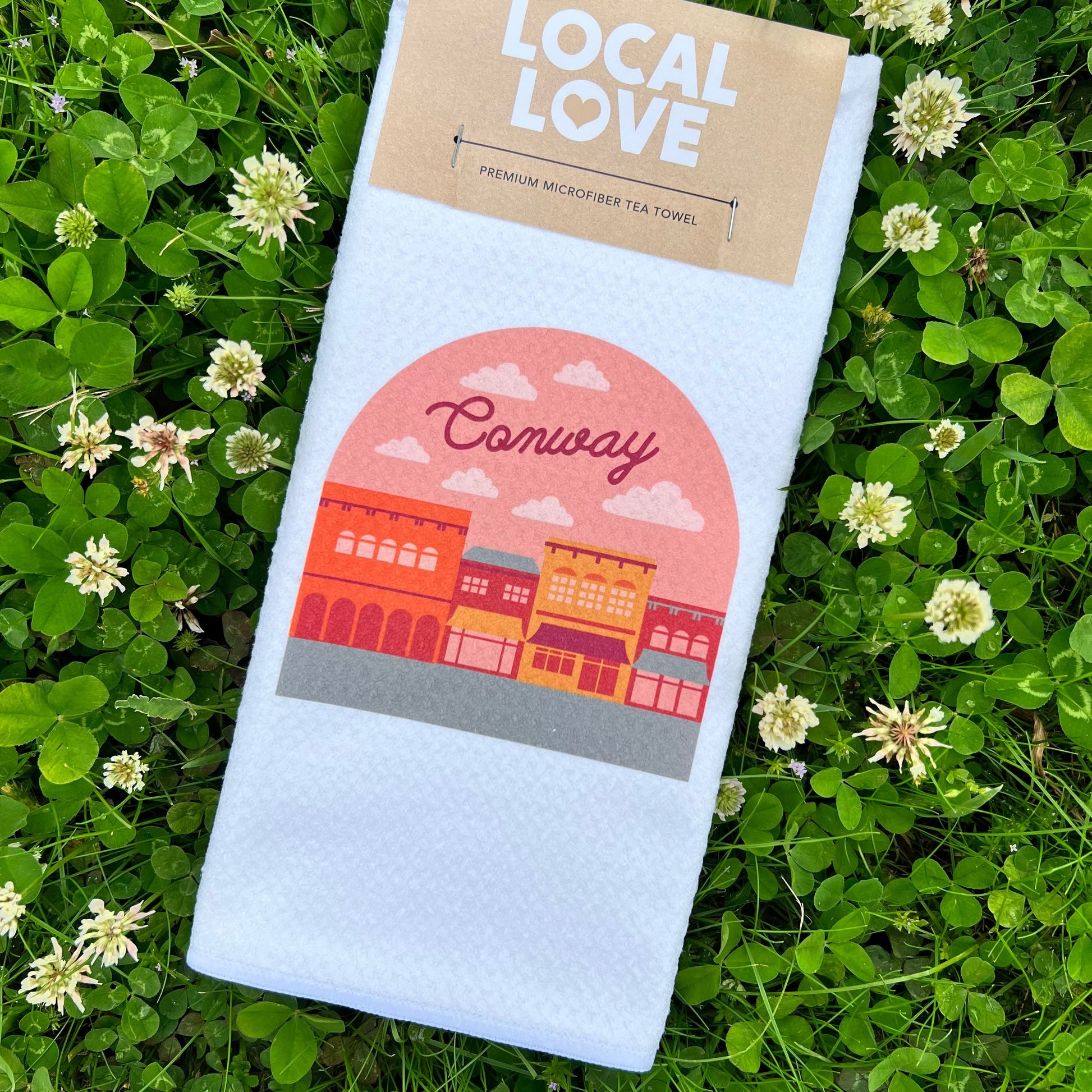 white towel with graphic of a city and "conway" printed on it laying in a field of clovers.