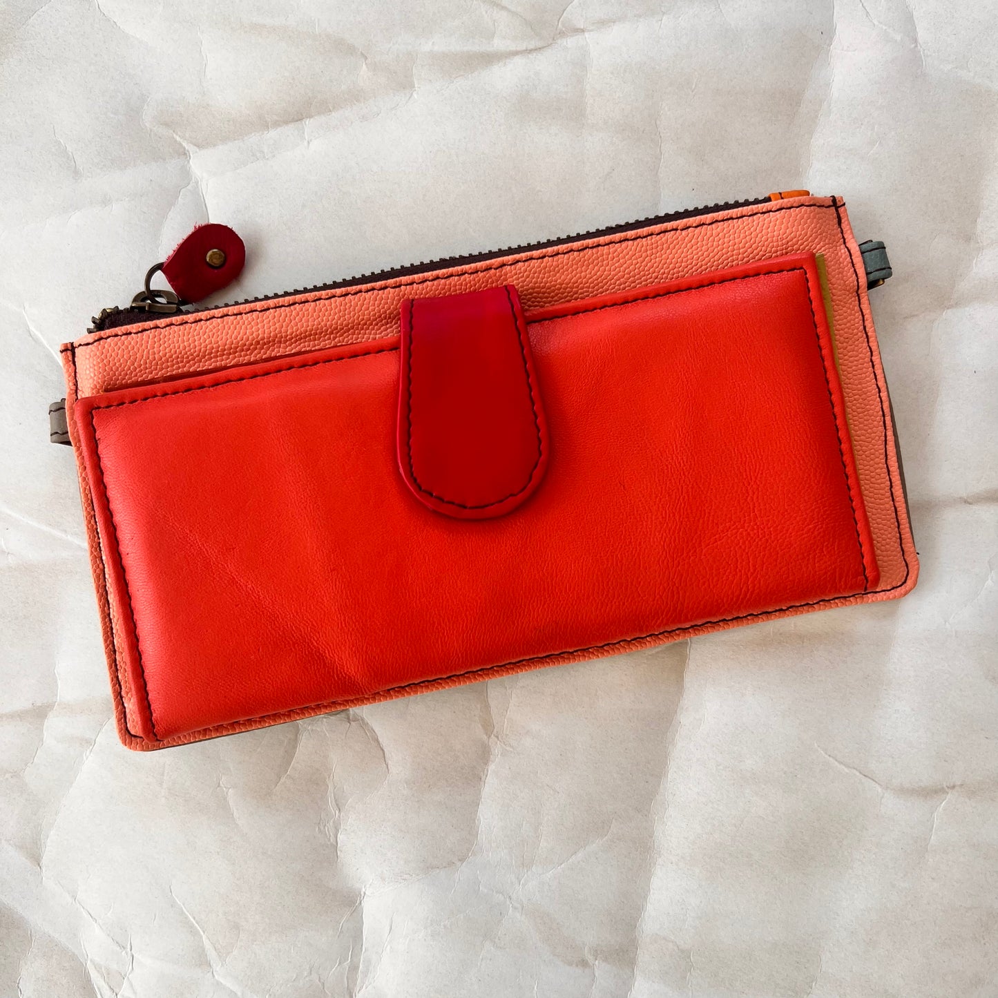 rectanglar kimber peach wallet with coral pocket and red tab closure.