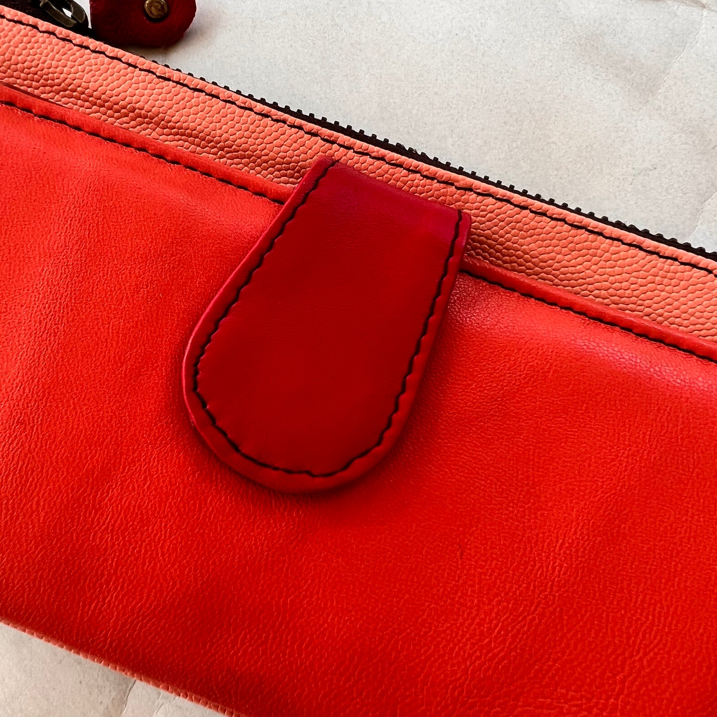 close-up of rectanglar kimber peach wallet with coral pocket and red tab closure.