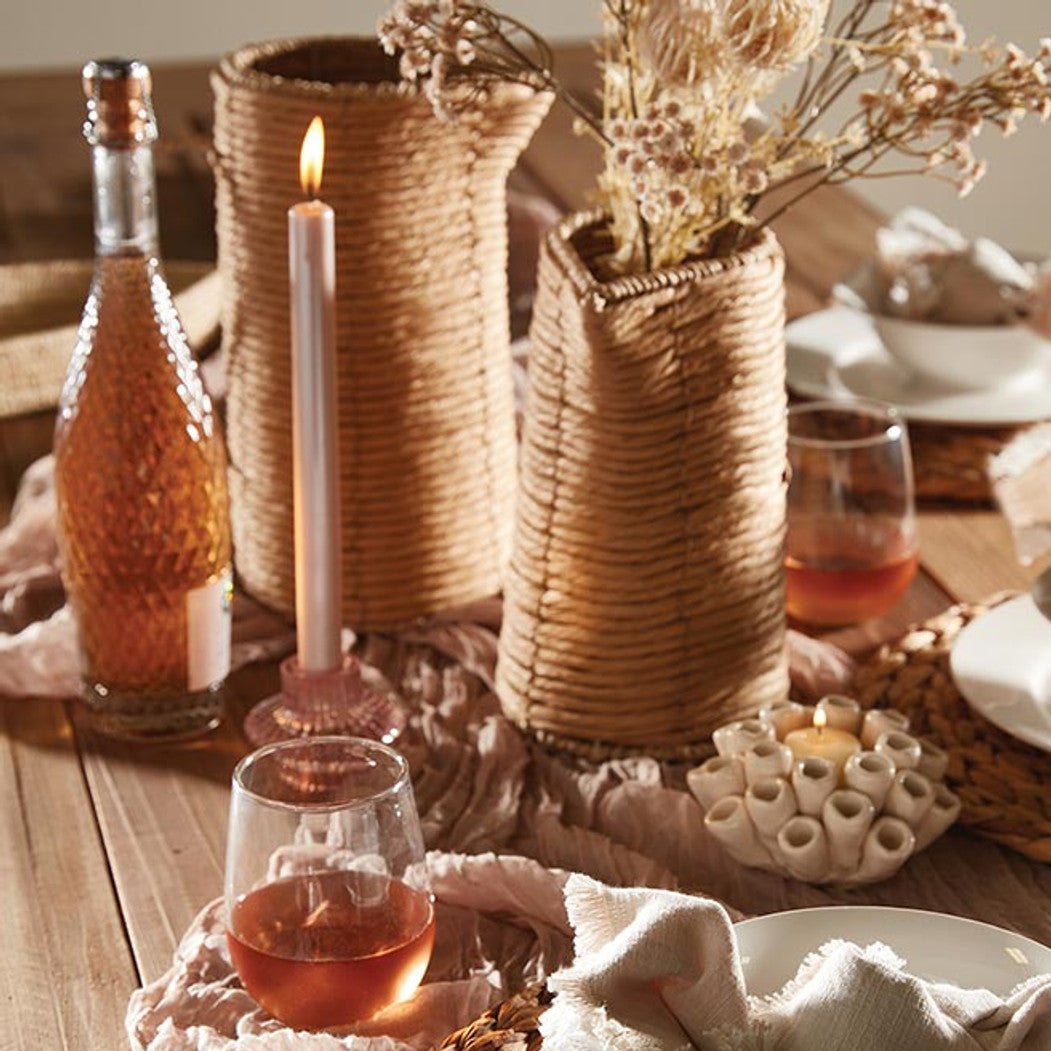 2 sizes of woven vases filled with dried botanicals set in the center of a table with candles.