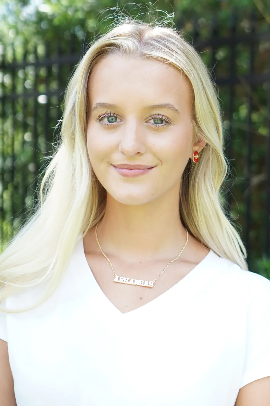 smiling person with long blonde hair wearing Arkansas Varsity Outline Necklace with a white t shirt