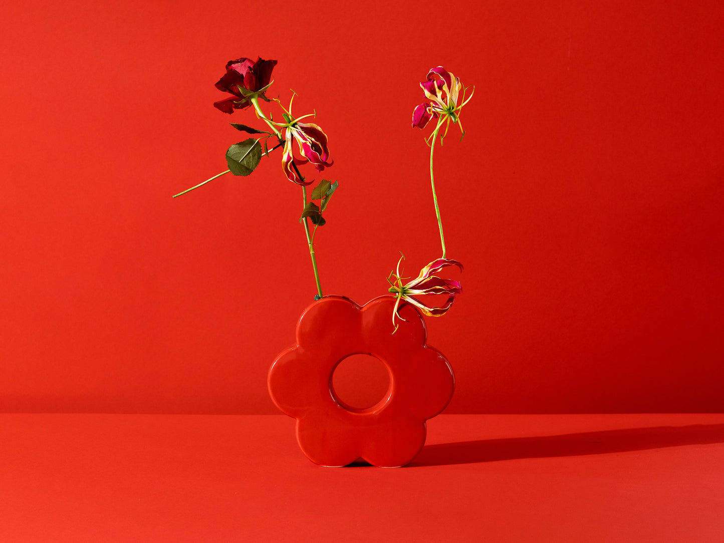 red flower shaped vase with an eclectic arrangement in it.