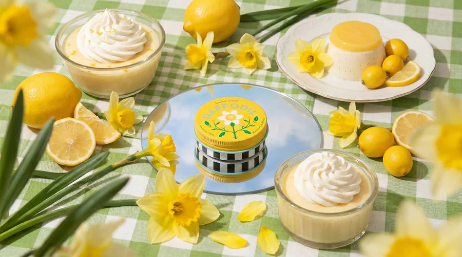 tin of daffodil lip balm set on a green gingham picnic blanket with lemons and flowers