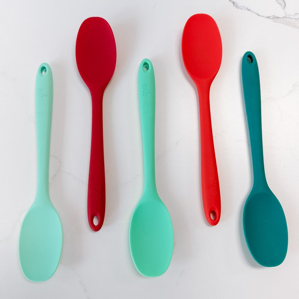 5 colors of mini silicone spoons arranged on a marble background.
