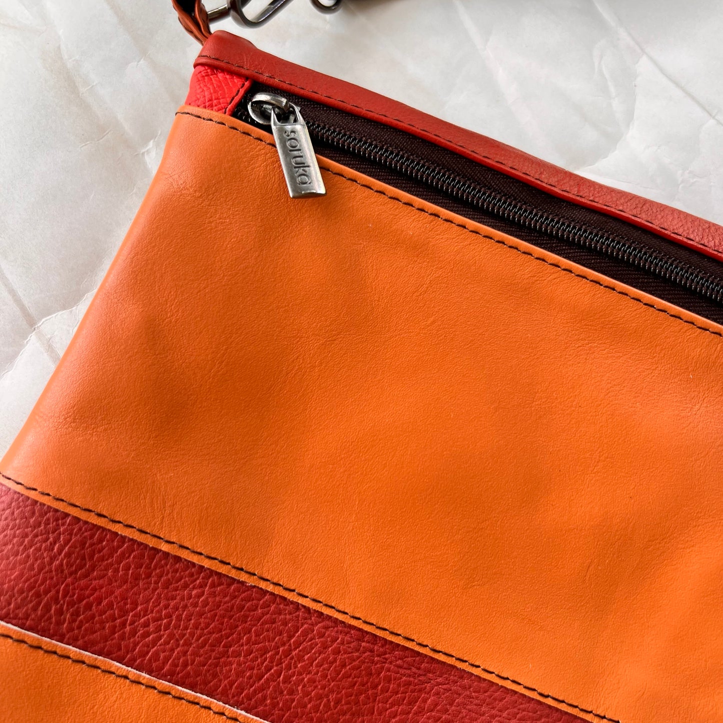 close-up of shades of orange striped greta bag with zipper across the top.