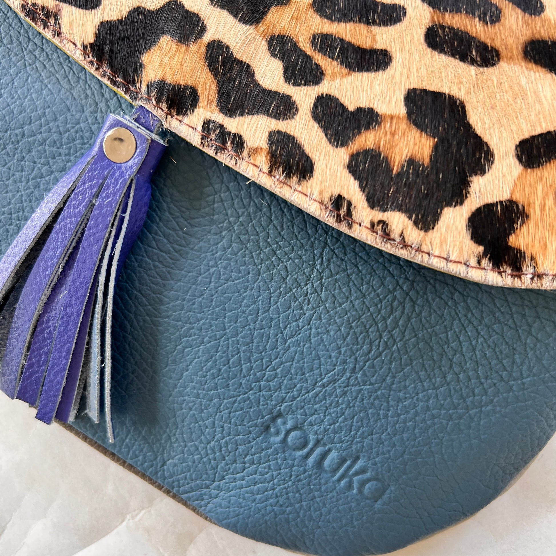 close-up of lola bag with cheetah print hair-on-hide flap with royal tassel over a teal body..