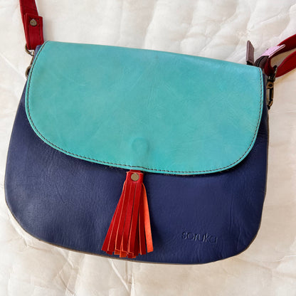 lola bag with turquoise flap with rusty colored tassel over a navy body.