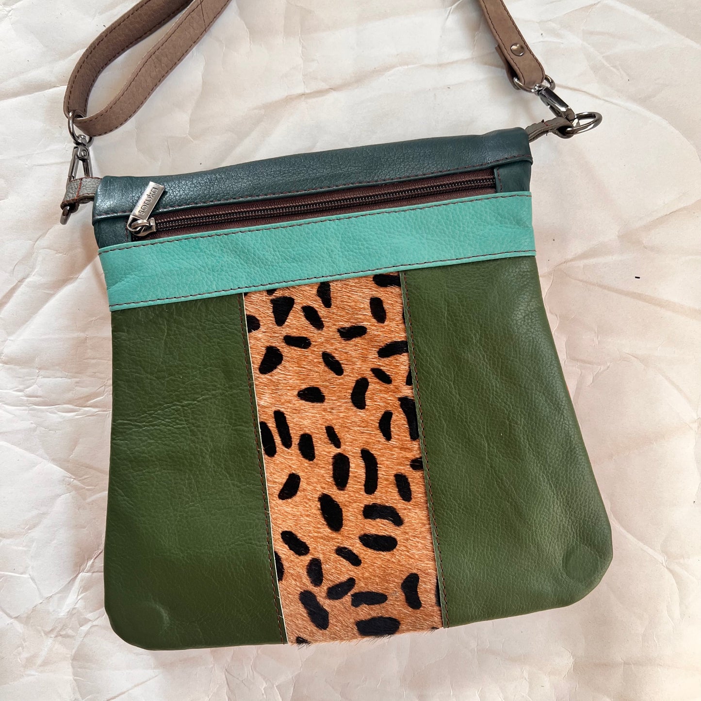 green greta bag with animal print block in the center with turquoise stripe and zipper across the top. 