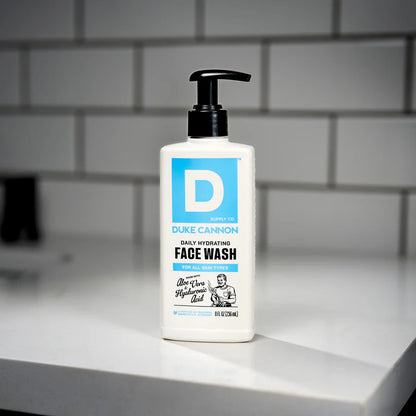 Duke Cannon face wash bottle on a bathroom counter with tiled wall background