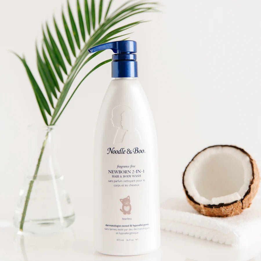 Bottle of Noodle & Boo newborn 2-in-1 hair and body wash with a coconut and palm leaf on a white background