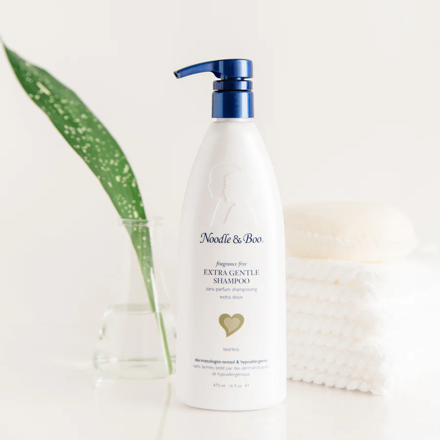 Bottle of Noodle & Boo shampoo with a green leaf and a stack of towels on a white background