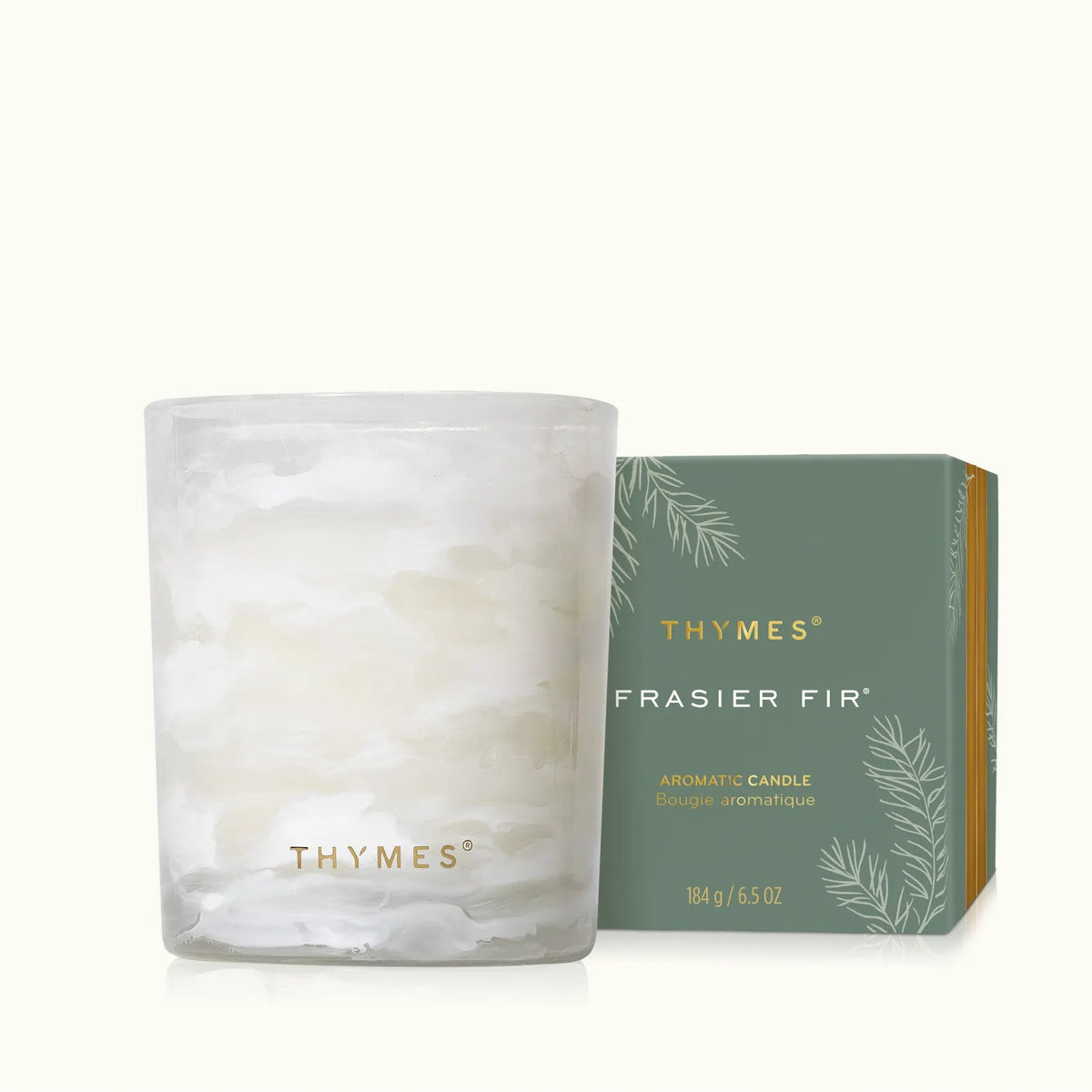 A frosted glass candle jar with white wax sits beside its green and gold Thymes Frasier Fir packaging box on a clean off-white background.