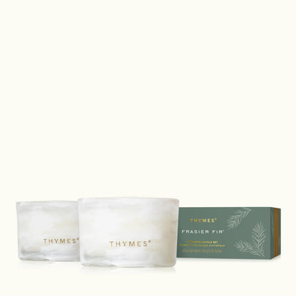 Two frosted glass candle jars with gold THYMES branding are shown in front of a muted green THYMES FRASIER FIR candle box on a clean off-white background.