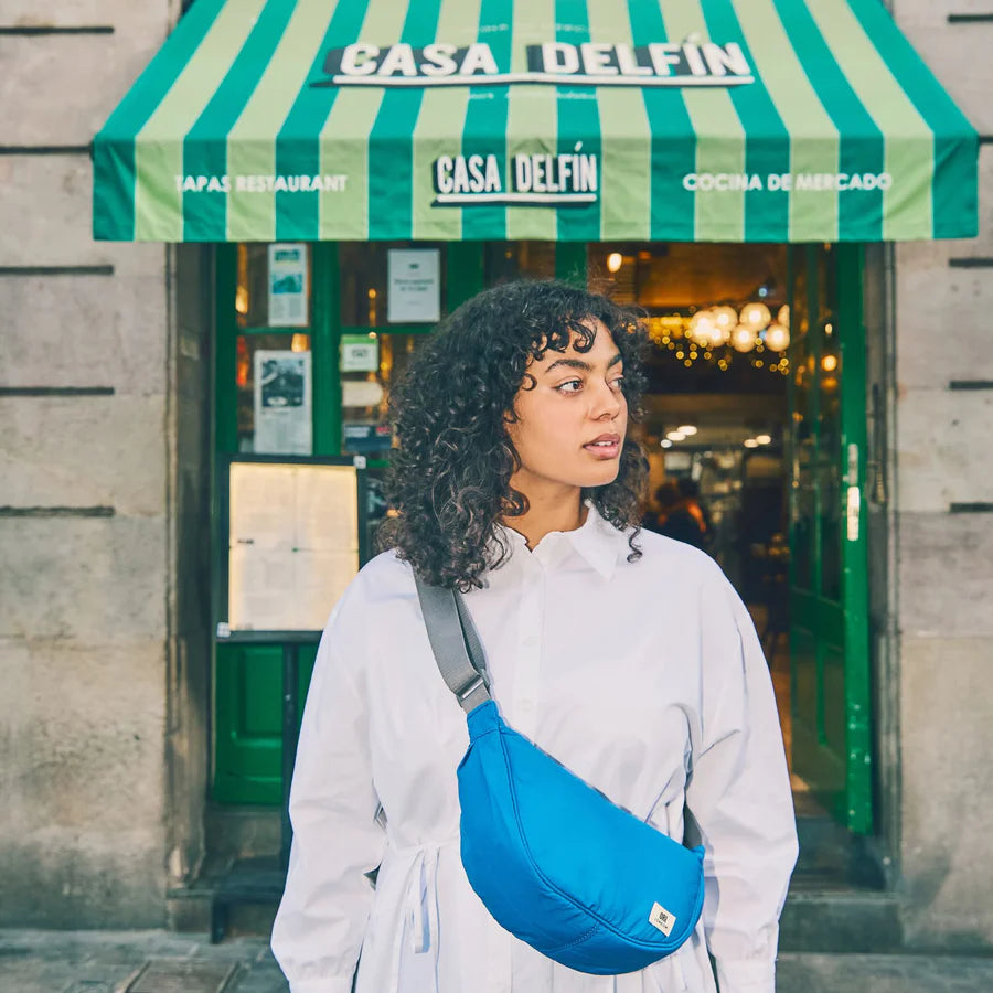 person with a blue bag standing in front of a restaurant with a green and white striped awning.