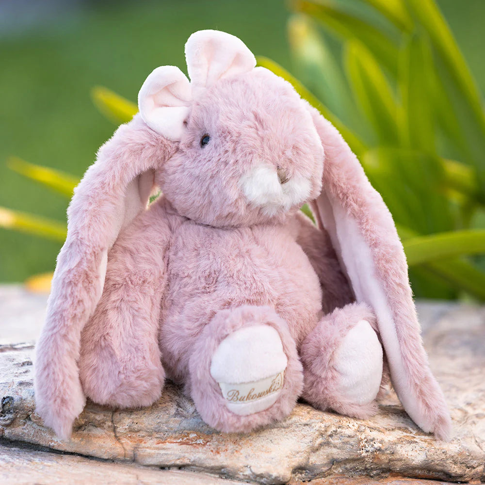 pink plush bunny sitting on a rock outdoors