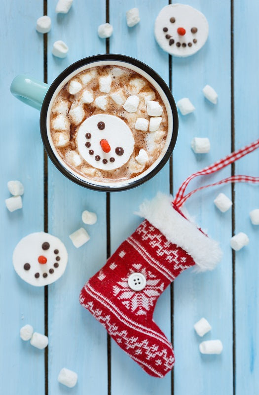 Hot chocolate with marshmallows  on a blue wooden surface with a red Christmas stocking.