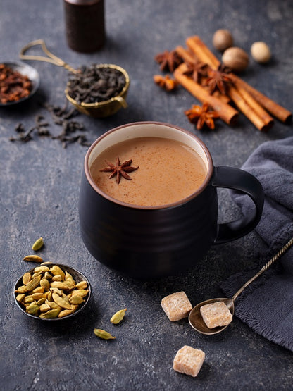 black mug filled with vanilla chai  set on a table surrounded by spices.