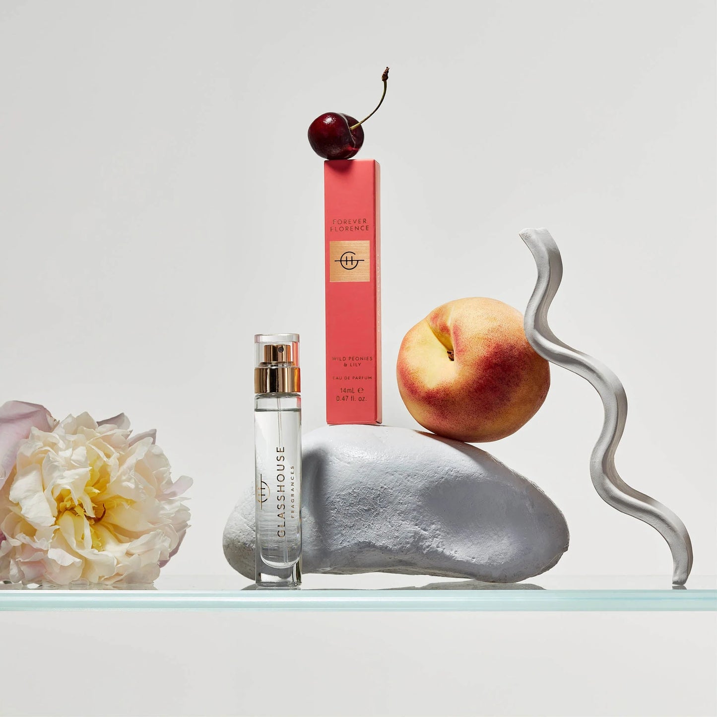 Forever Florence Eau De Parfum and its box arranged with a flower, a cheery, and a peach on a rock.