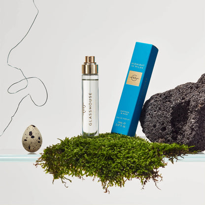 Midnight in Milan Eau De Parfum and its box arranged with and a speckled egg, moss, and lava rock.