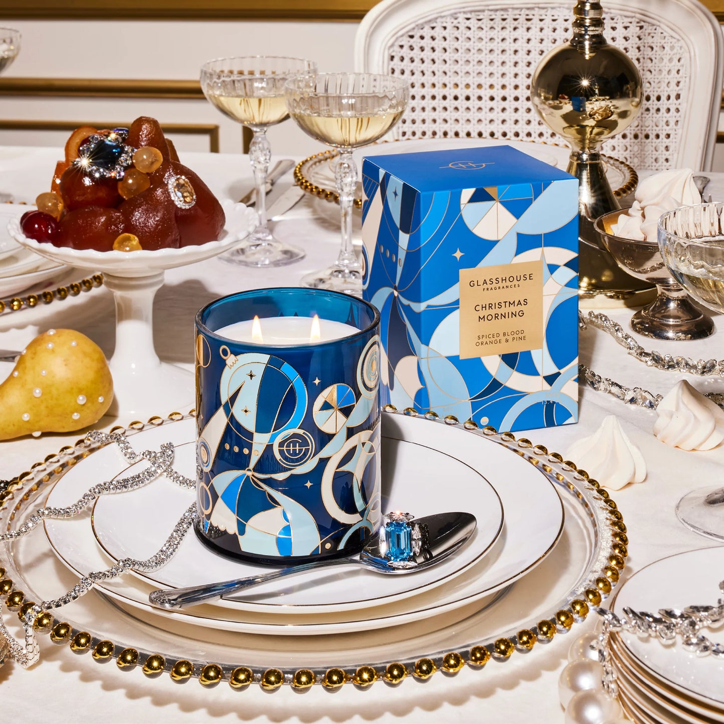 Table arranged with dishes and glasses and plates of food with a Christmas morning candle, lit and set on a stack of plates.