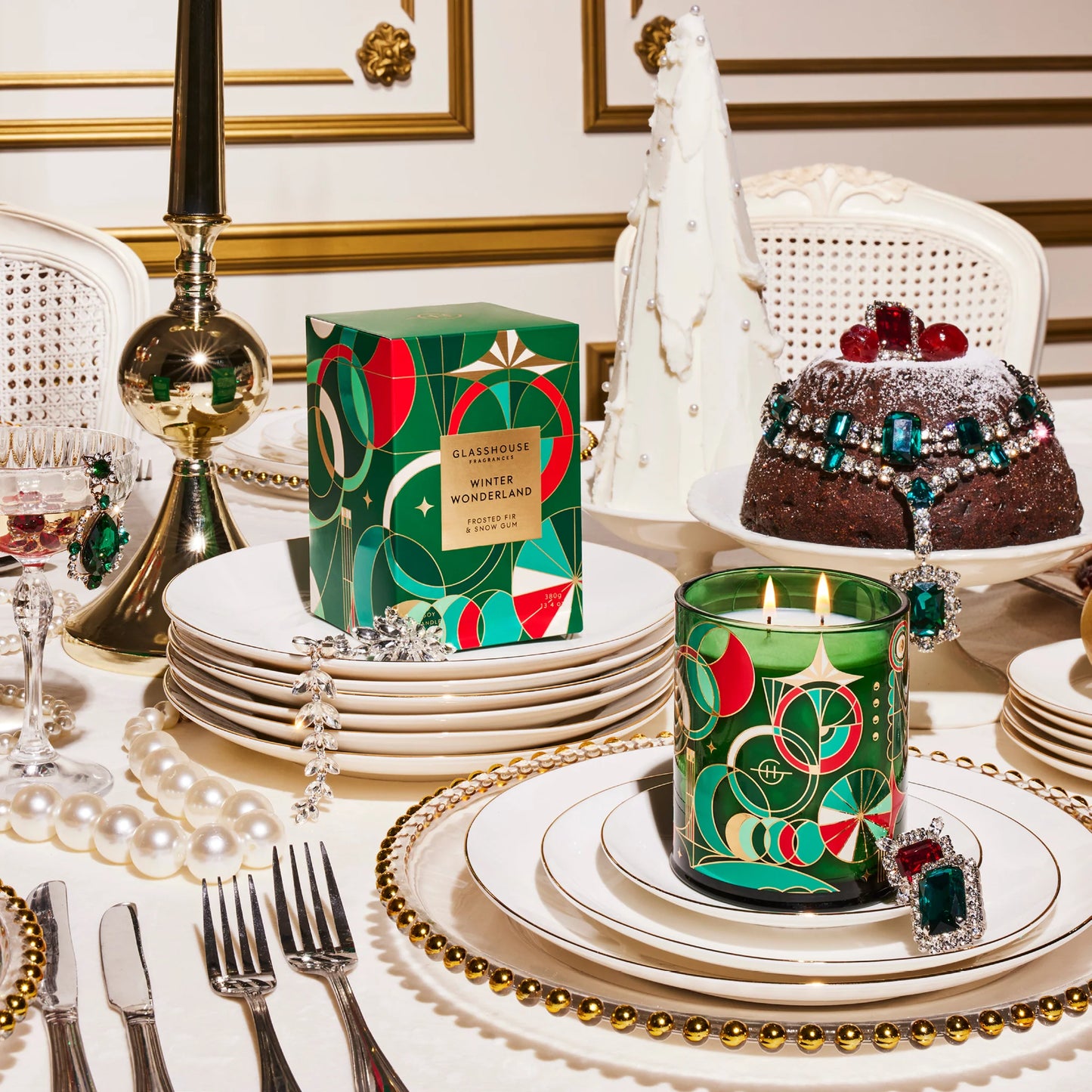 table set with stacks of dishes and a cake in the background with a it winter wonderland candle set on plates.