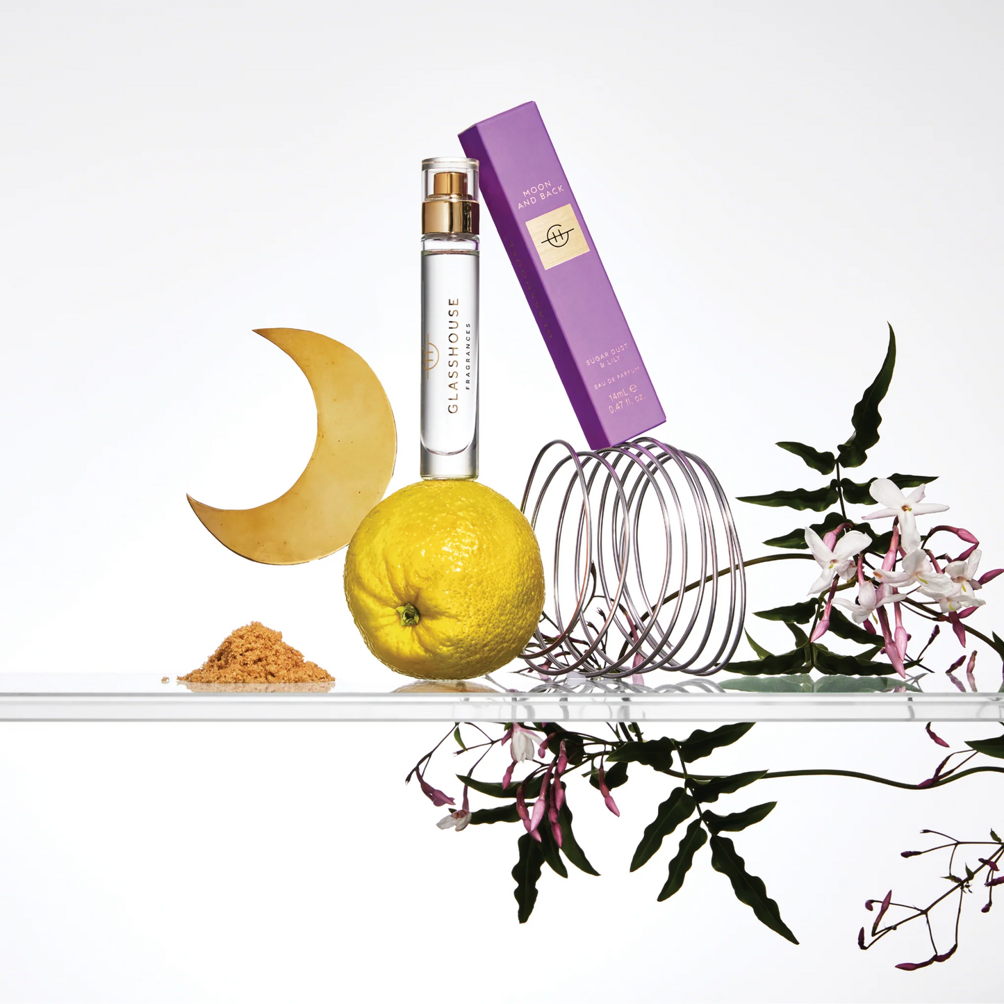 Moon and Back Eau De Parfum and its box arranged with flowers, a lemon, brown sugar, and a cresent moon shape.