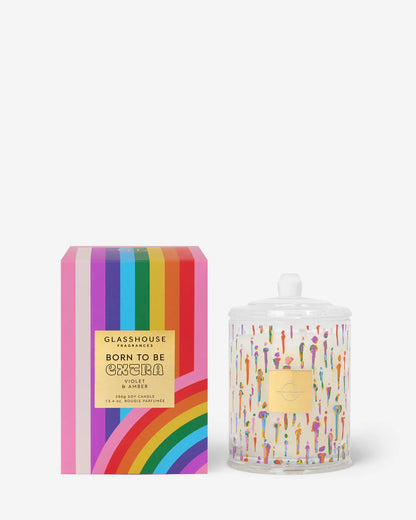 Glasshouse Candle Co candle with colorful design of different people printed on its glass vessel set next to its rainbow striped packaging