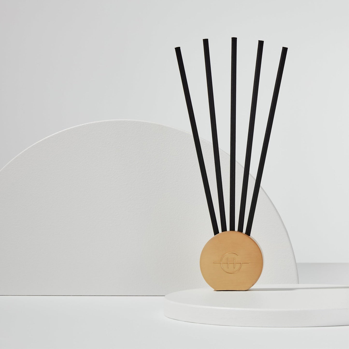 Gold Scent Scene Metal Vessel filled with scent stems and displayed on a white surface in front of a white half circle