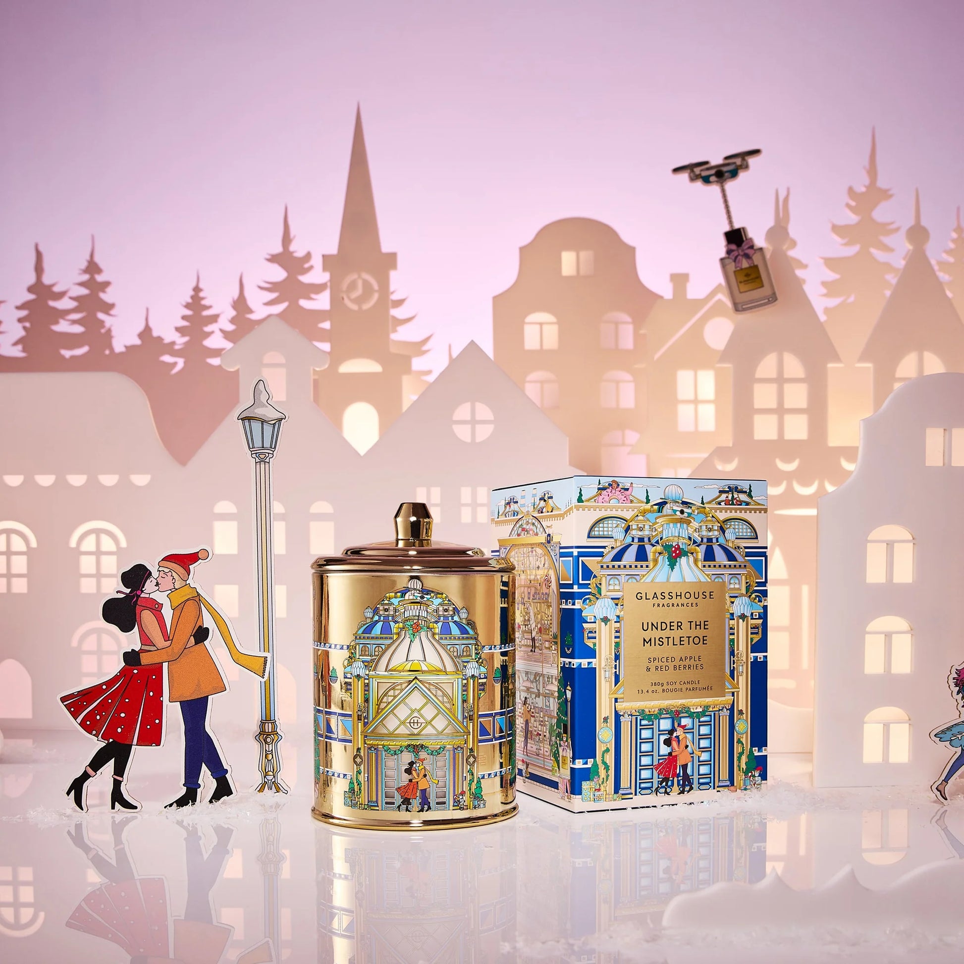 Under The Mistletoe Candle set next to its box packaging with a city skyline background