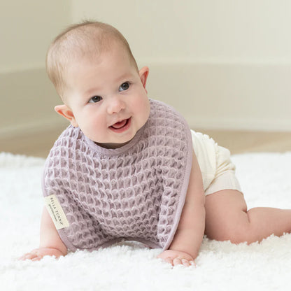 baby crawling on a white rug wearing orchid bib.