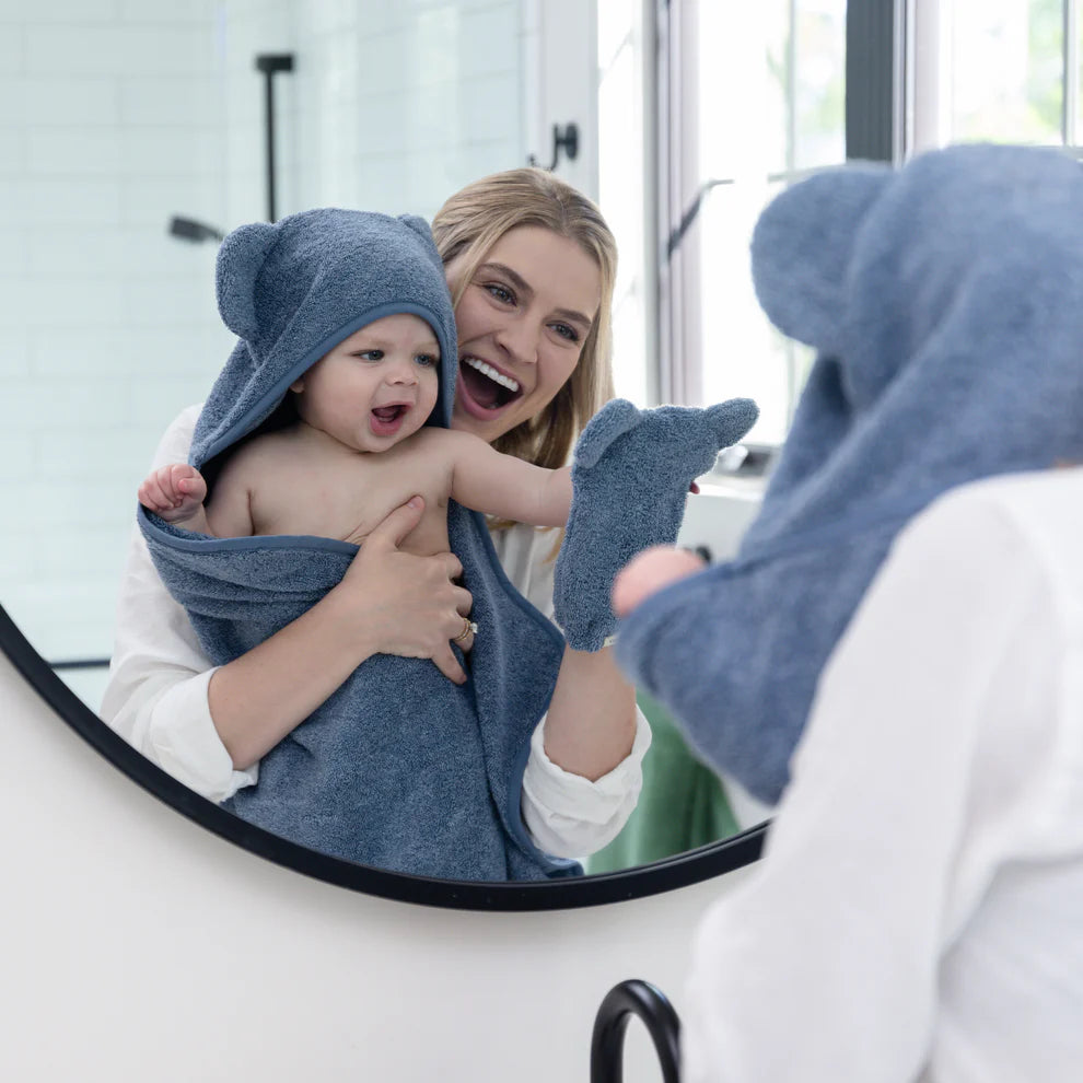 person holding baby wearing rain towel and holding mitt.