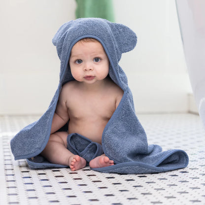 baby sitting on bathroom floor wearing rain towel with hood on.