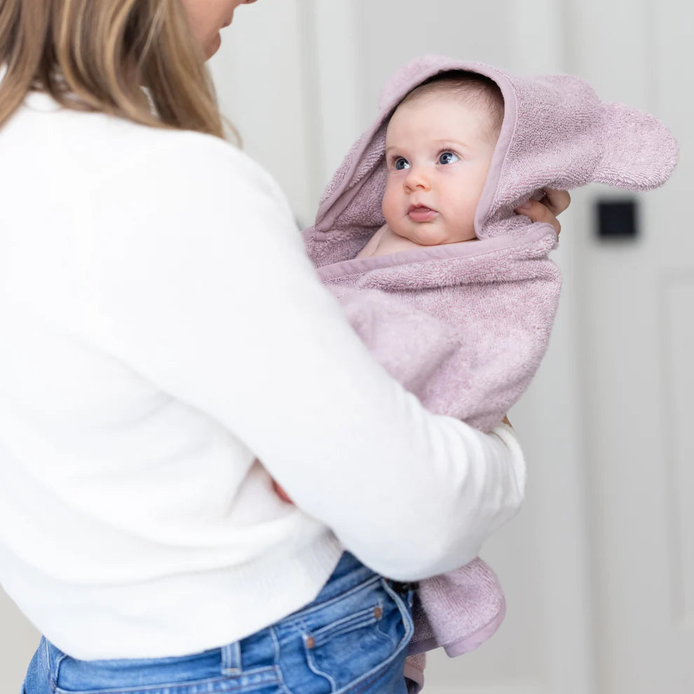 person holding baby wrapped in orchid hooded towel.