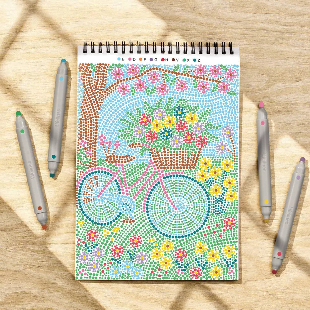 Coloring book with a bicycle and floral design on a wooden surface with coloring pencils.