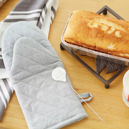 Gray oven mitts on a wooden surface with cake tester and baked cake