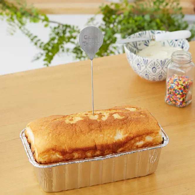 cake in a tin with a cake tester in it on a wooden table.