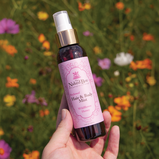 hand holding bottle of wildflower hair and body mist in front of a meadow of flowers