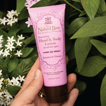 Jasmine & Honey hand and body lotion held in front of a jasmine plant